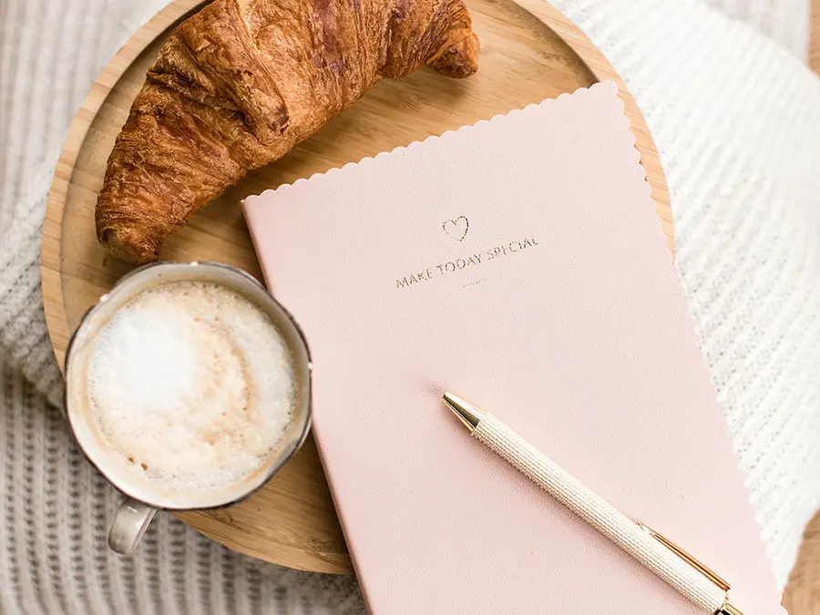 Notebook met pen en cappuccino op een houten dienblad – een moment van reflectie en inspiratie