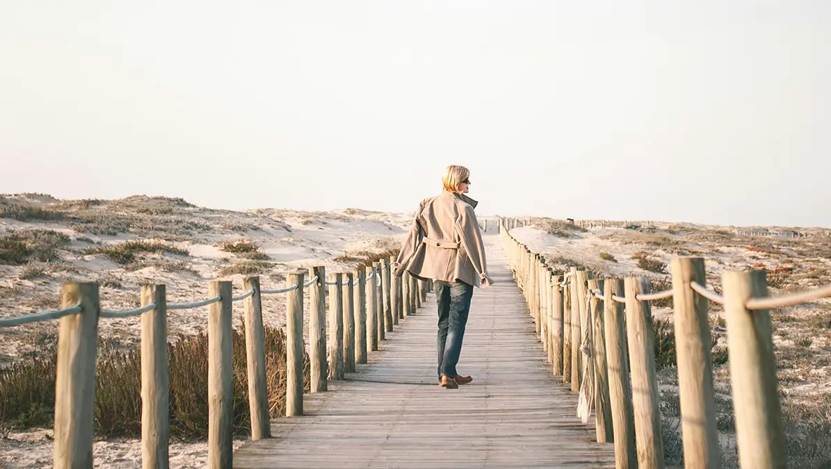 Vrouw loopt over een houten pad in een open landschap, symbool voor het zetten van een nieuwe stap en het kiezen van haar eigen pad in werk en leven