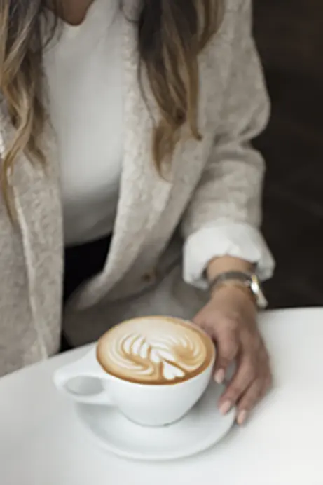 Vrouw in een rustige setting met een cappuccino, genietend van een moment van helderheid en ontspanning.