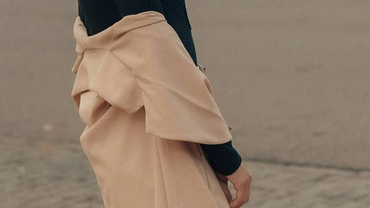 Vrouw trekt buiten langzaam haar jas uit als symbool voor stoppen met aanpassen en kiezen voor vrijheid in werk en leven.