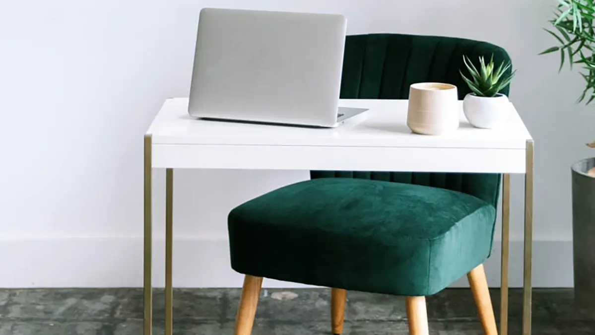 Stijlvol licht thuiskantoor met groene stoel, laptop en planten – rustige plek voor reflectie en schrijven.