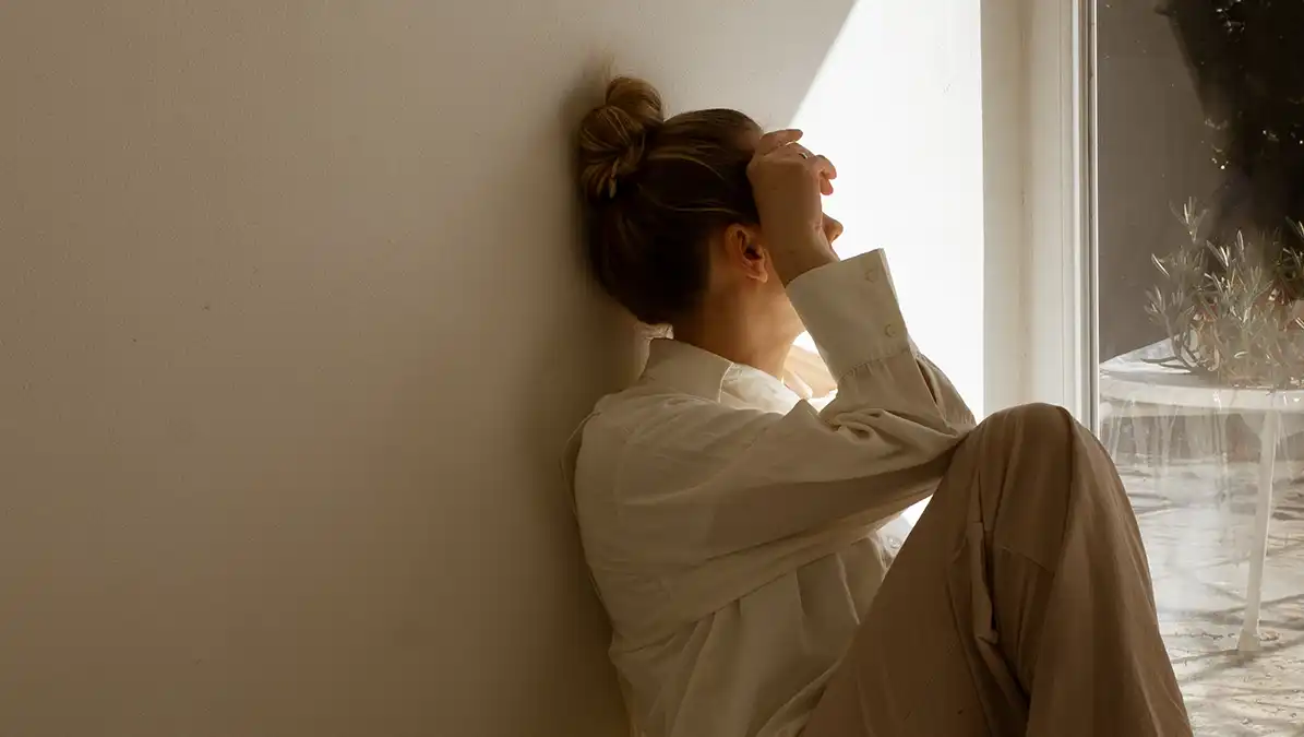 Vrouw zit op de grond bij een raam en kijkt in het zonlicht naar buiten denkend over haar werkleven, haar loopbaan